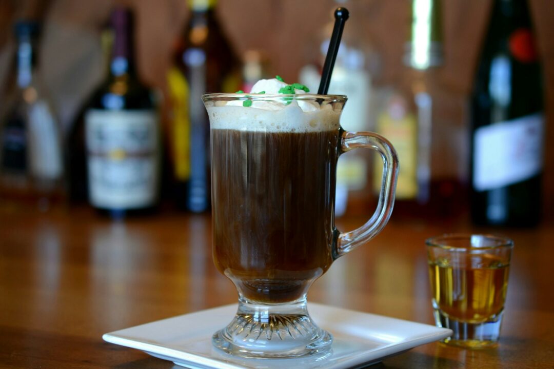 Irish Coffee cocktail Irish Whiskey in shot glass for St. Patty's Day on wooden bar liquor bottles